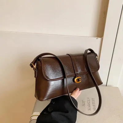 A brown leather shoulder bag held up against a white wall